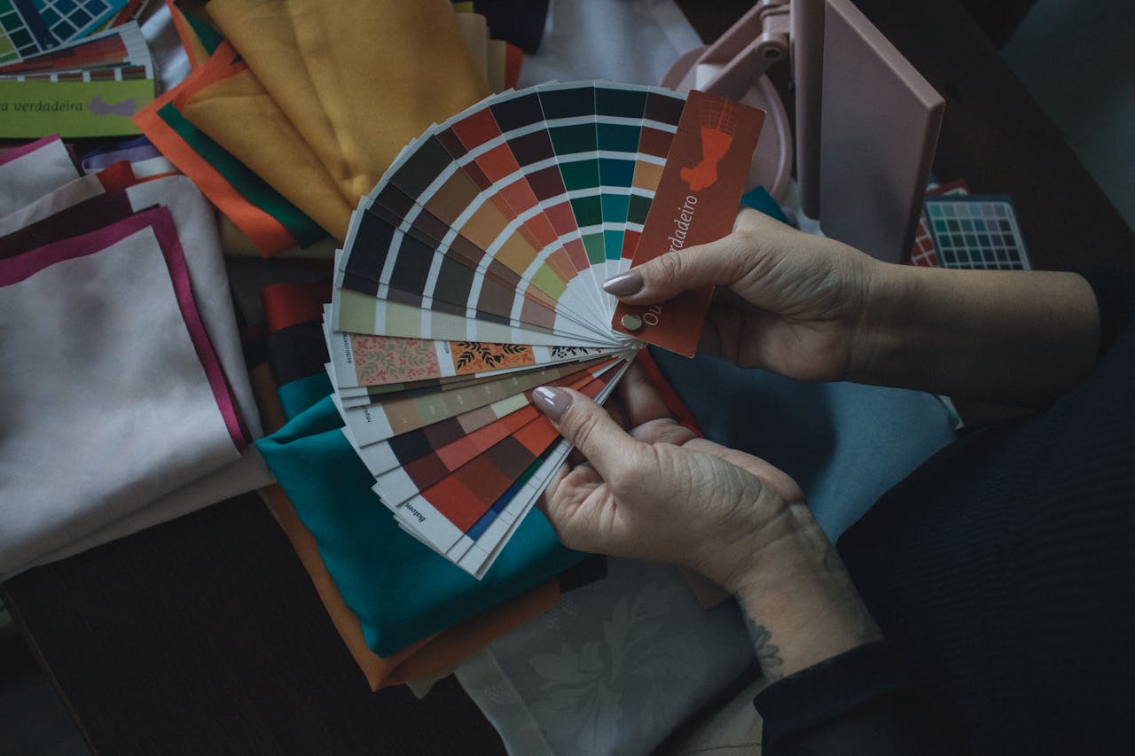 Hands holding color swatch above fabrics. Ideal for design, fashion, and color theory themes.